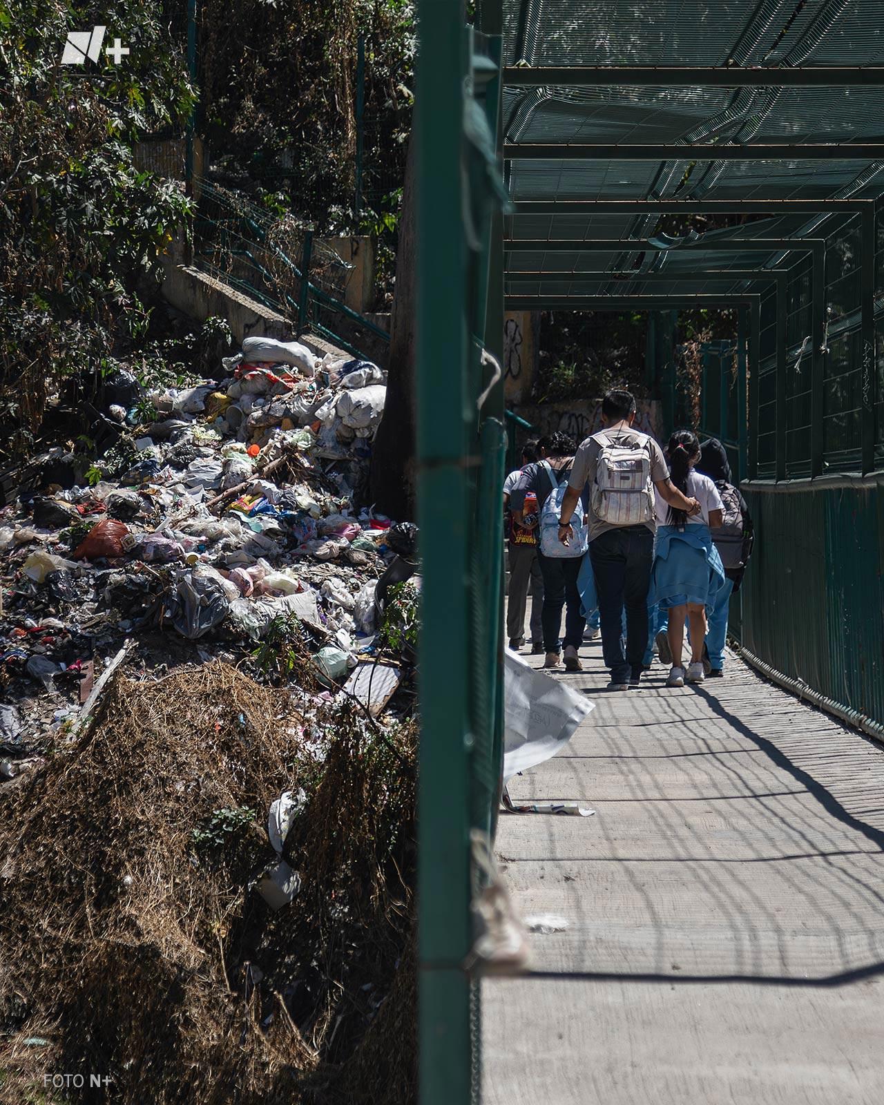 Niños junto a sus padres atraviesan un puente rodeado de basura en la Ciudad de México