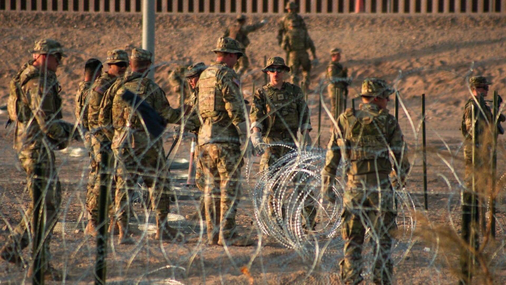 Elementos del ejército de EUA refuerzan con alambre con púas donde migrantes de diversas nacionalidades esperan.
