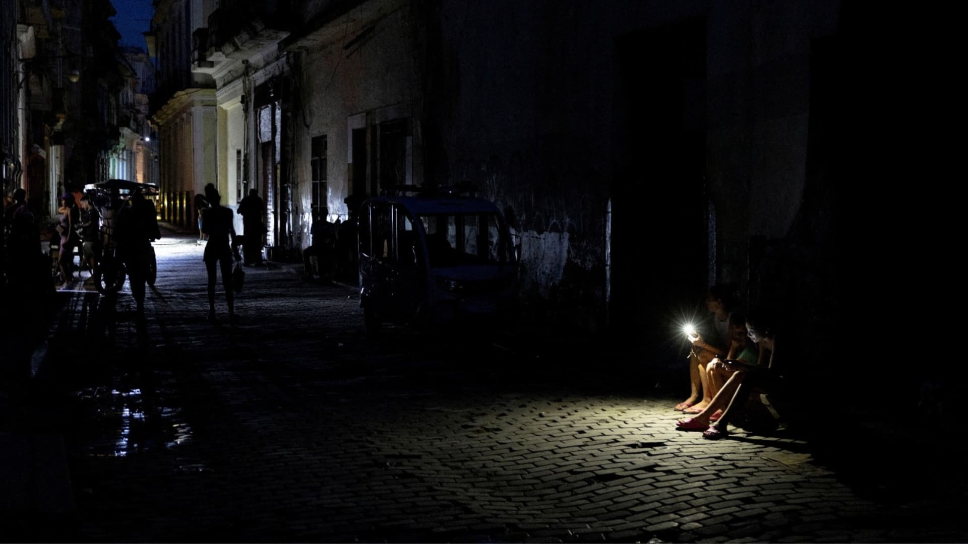 Varias personas se sientan en una calle oscura iluminada por la linterna de un teléfono móvil durante un apagón