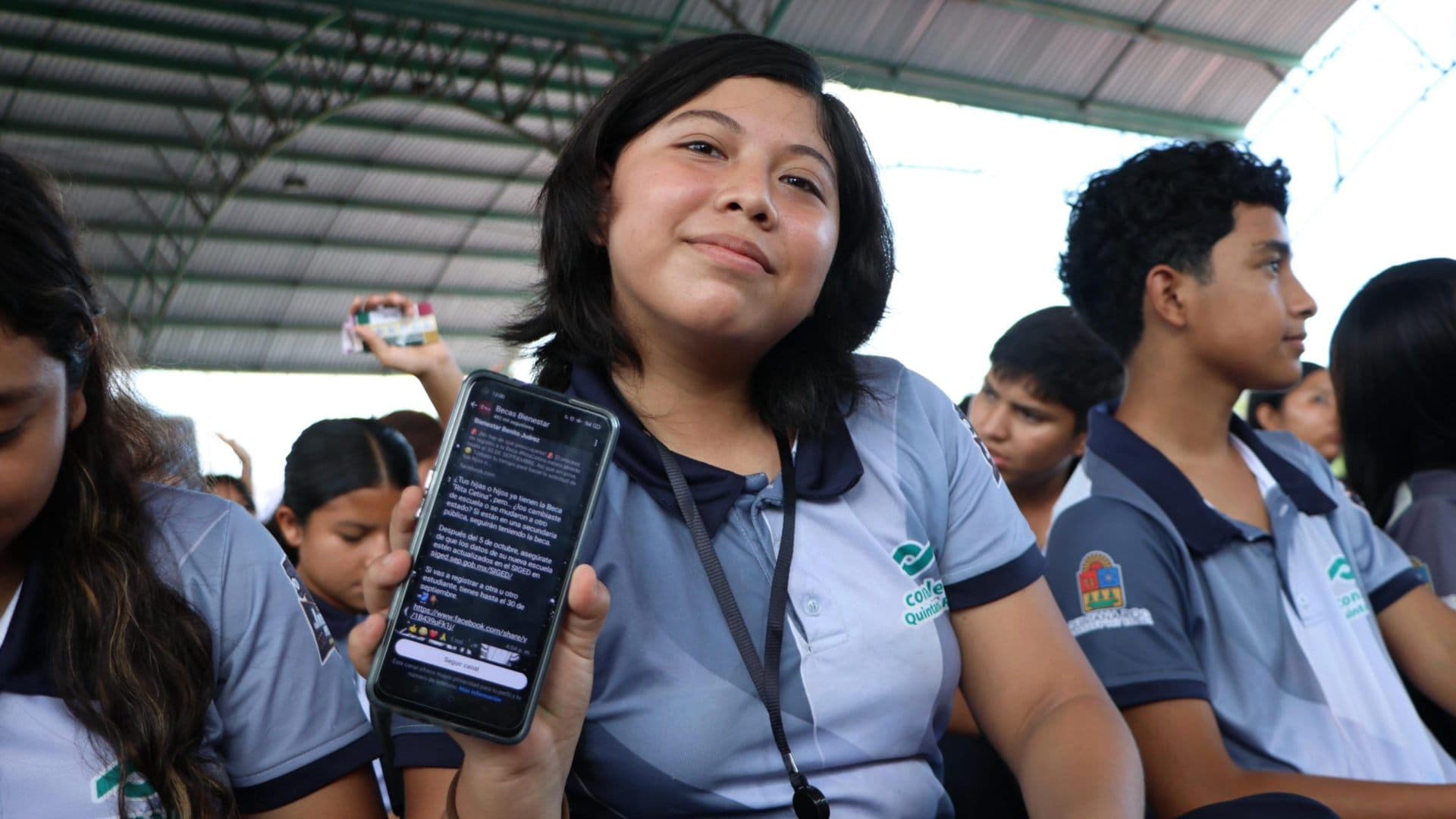 Estudiante sostiene celular. Dónde suspendieron Asamblea Beca Bienestar 2026.