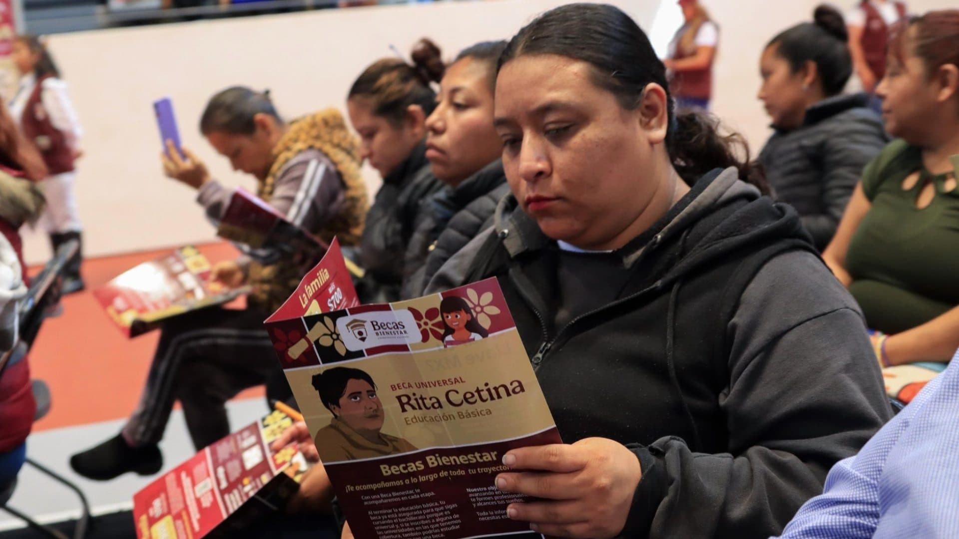 Mamá sostiene folleto de información de la Beca Rita Cetina.