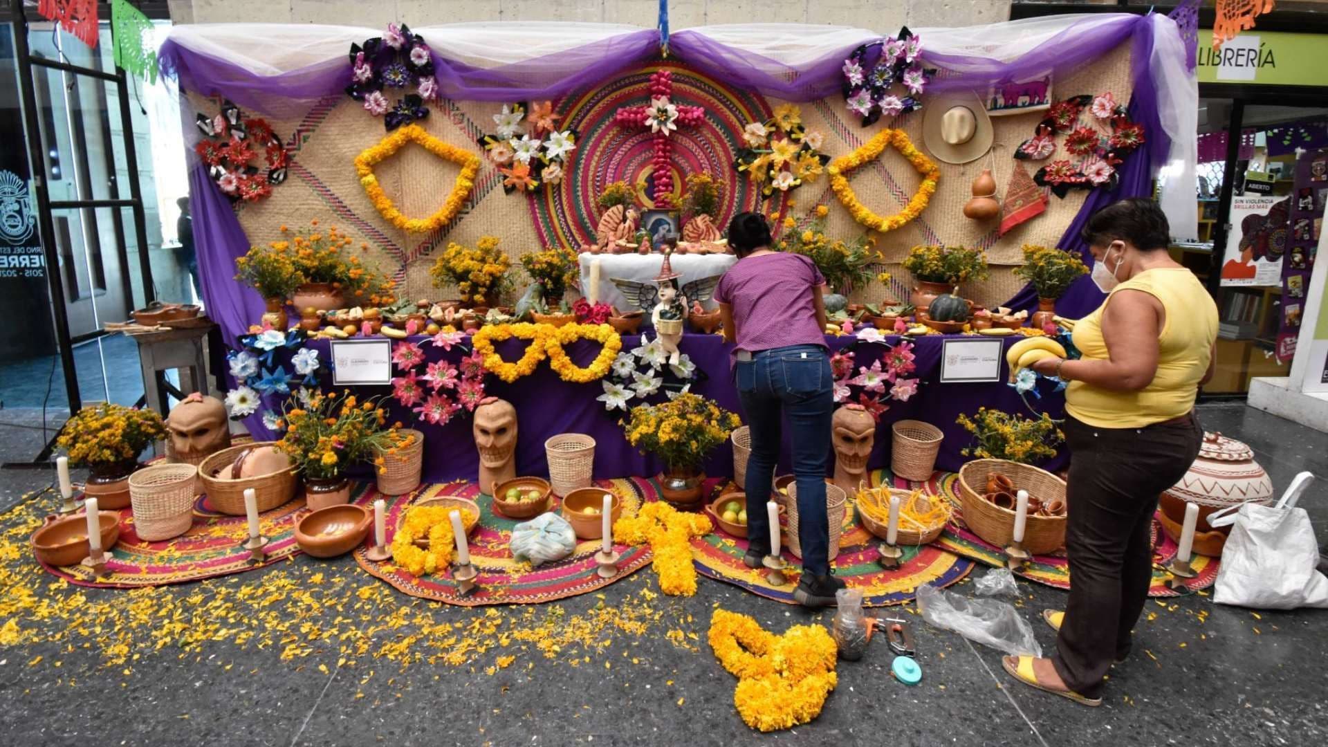 Mujeres instalan ofrenda de día de muertos. Qué día de pone el altar de Día de Muertos.