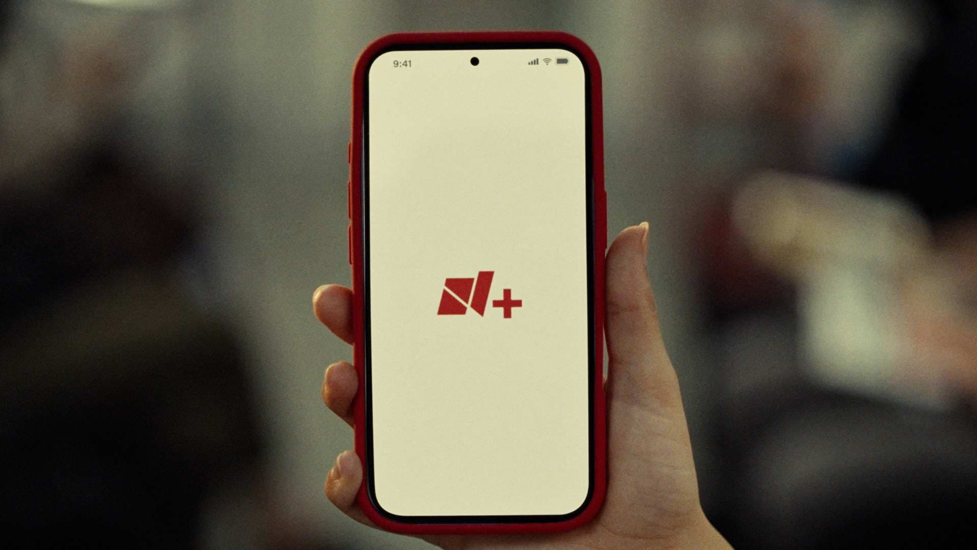 Mano sostiene celular con app y logo de Nmás. Nmás Lanza App en agosto 2026