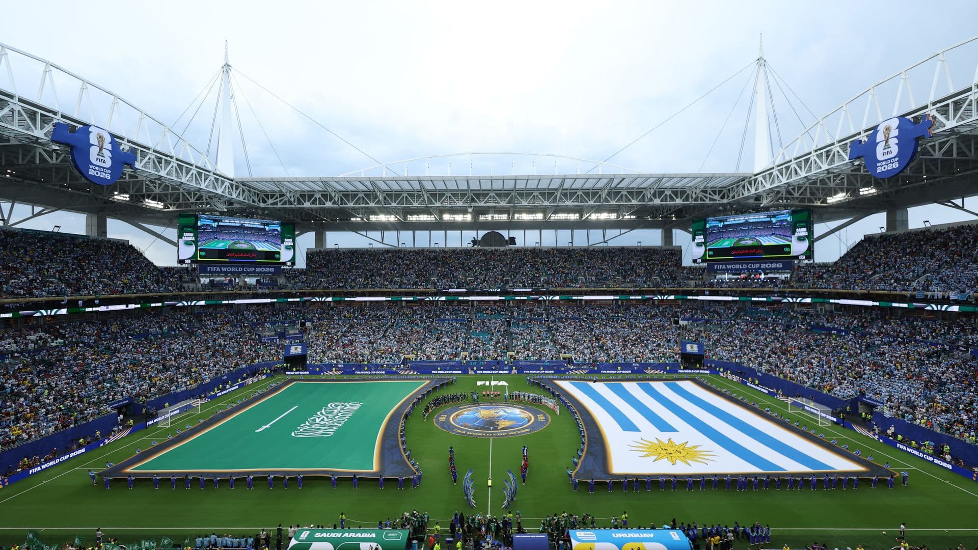 Voluntarios sostienen las banderas durante el protocolo de los himnos en el Mundial 2026; la insignia de Arabia Saudita no tuvo contacto con el terreno de juego.
