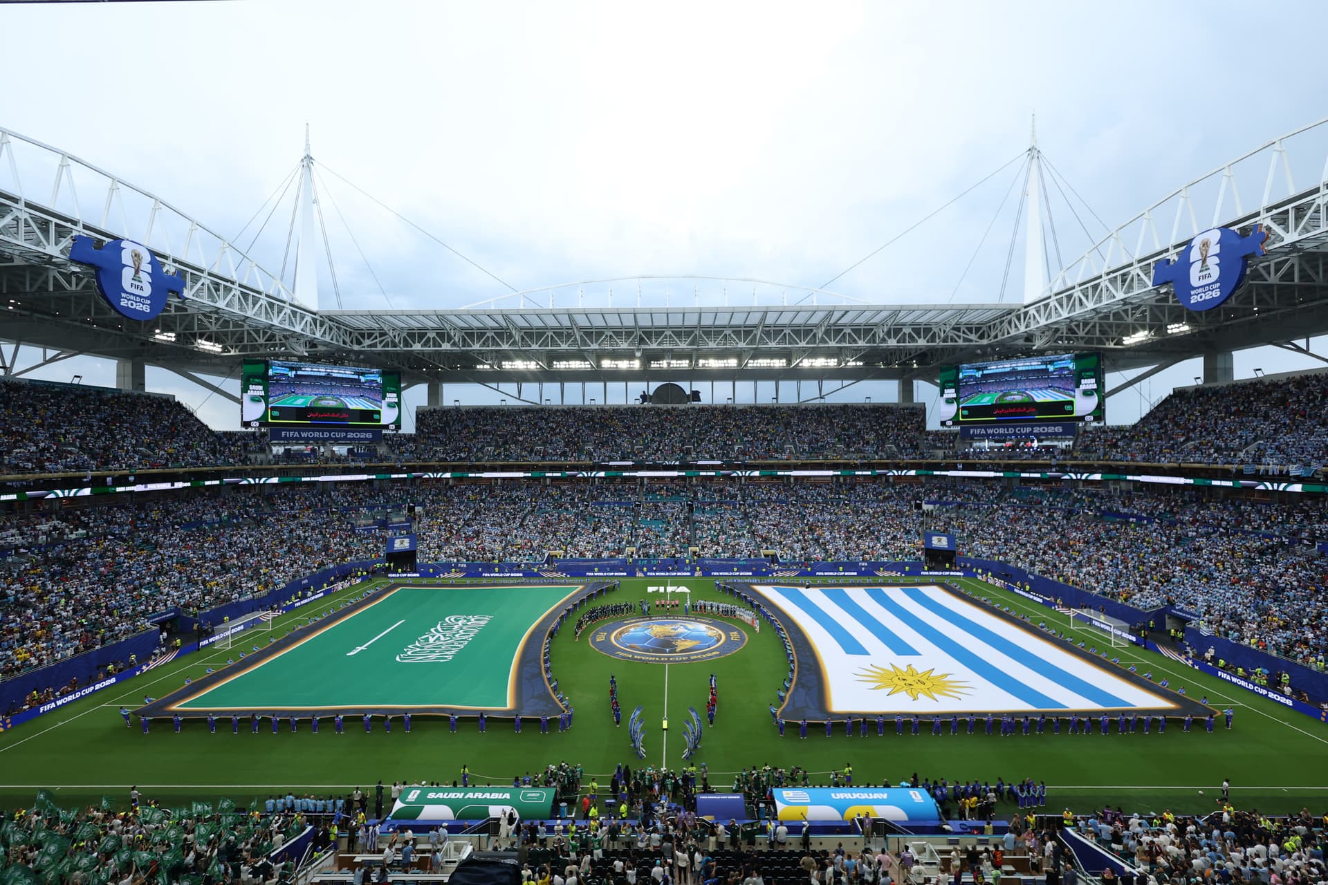 Voluntarios sostienen las banderas durante el protocolo de los himnos en el Mundial 2026; la insignia de Arabia Saudita no tuvo contacto con el terreno de juego.