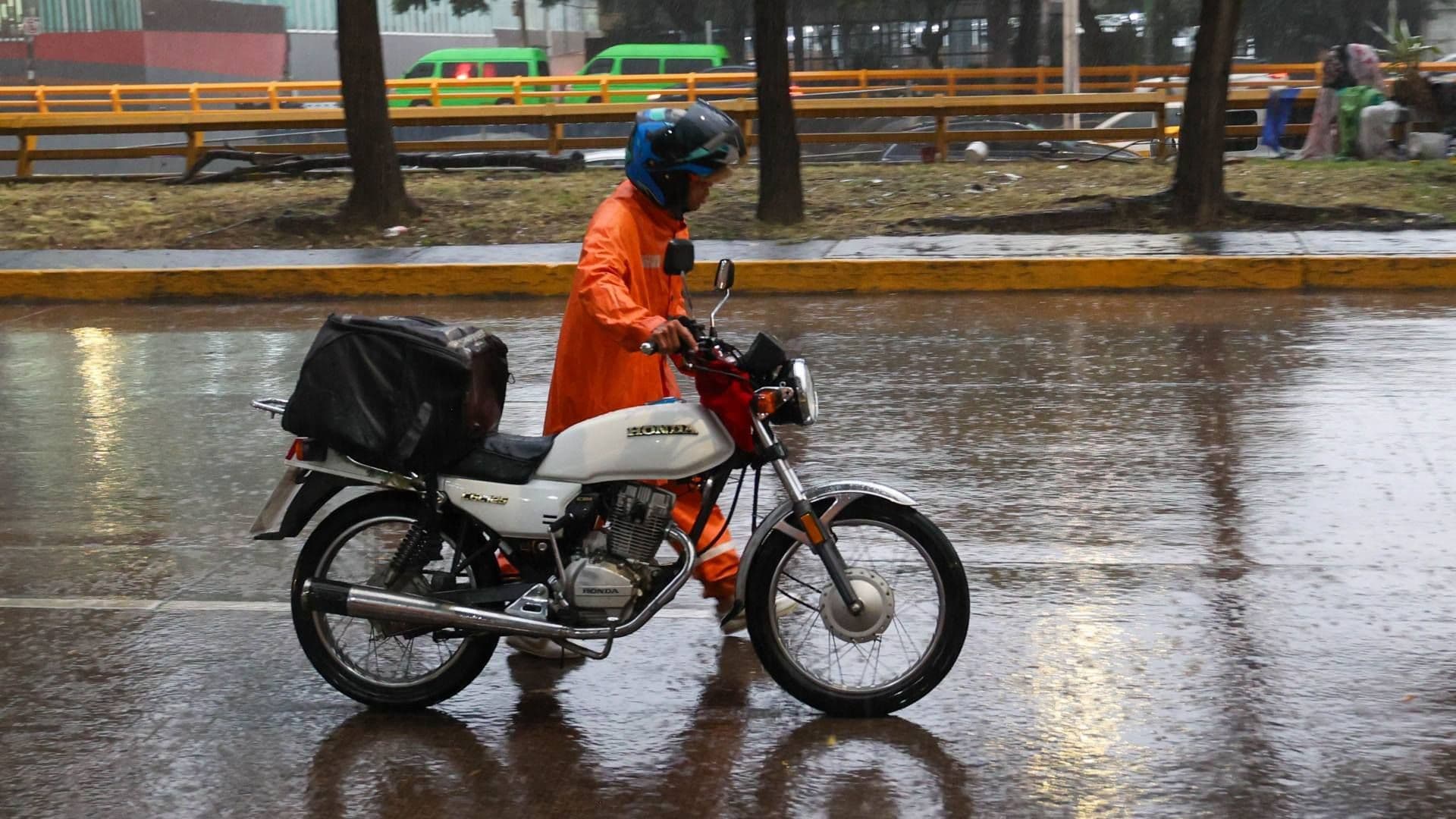 Un hombre camina junto a su moto y se protege de la lluvia en CDMX en agosto 2026. Foto: Cuartoscuro | Archivo