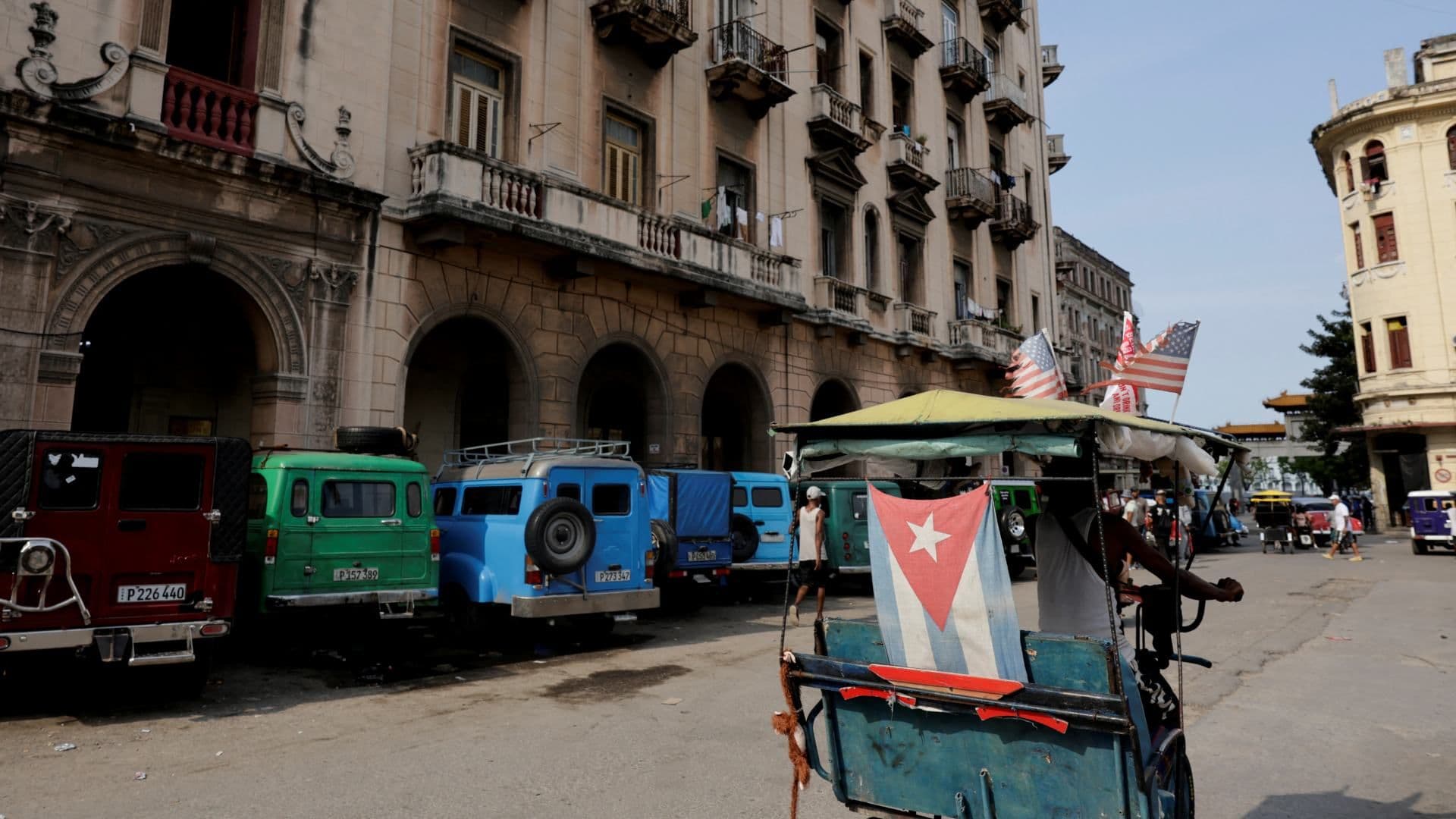Hombre conduce un bicitaxi junto a automóviles clásicos estacionados en Cuba, el 21 de julio de 2026. Foto: Reuters | Archivo