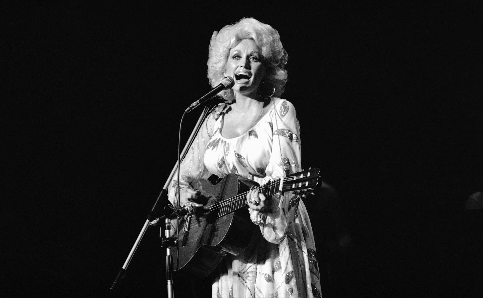 Dolly Parton cantando frente a micrófono y tocando la guitarra