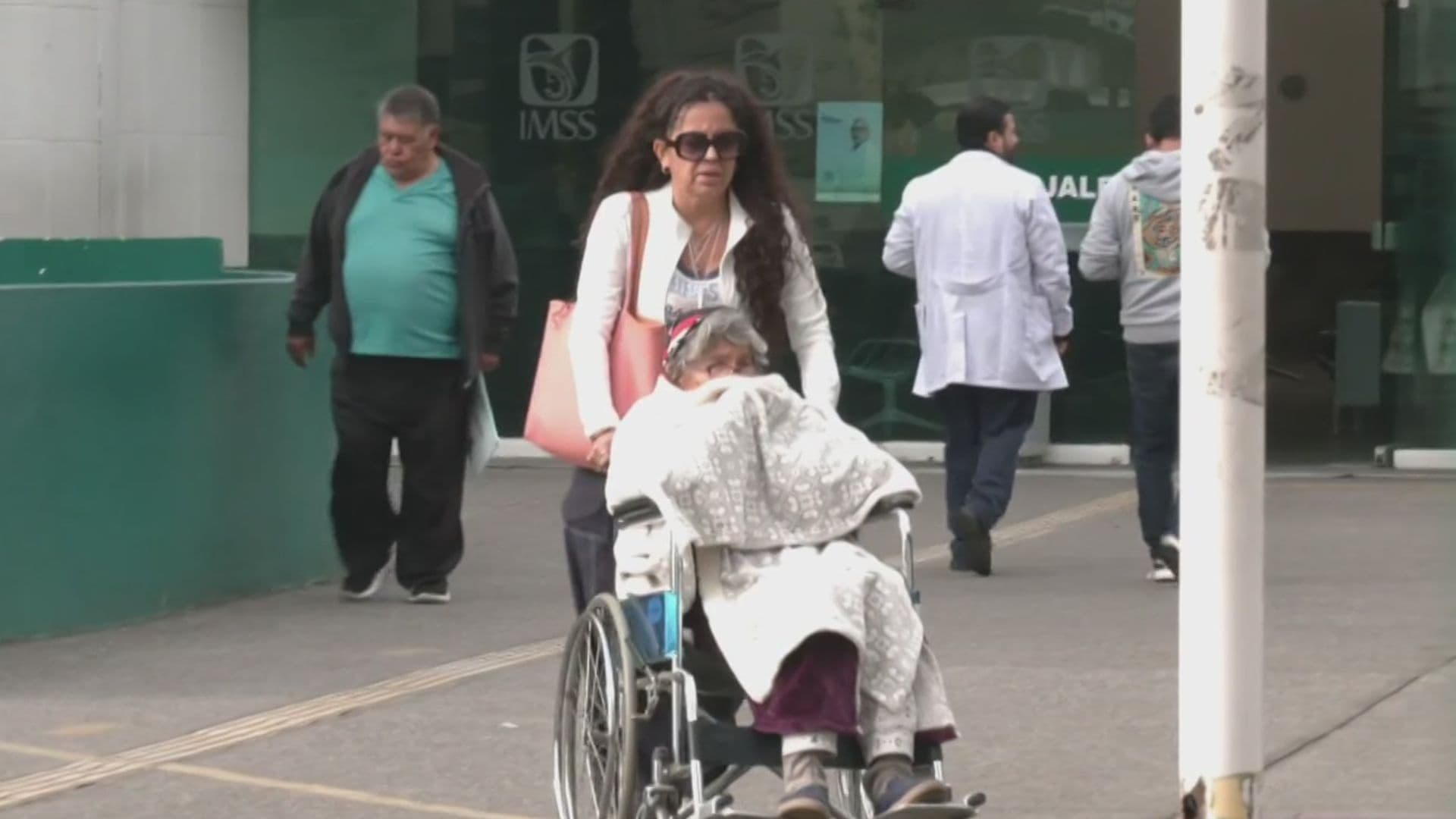 La señora Ebelia sale de una clínica en silla de ruedas.