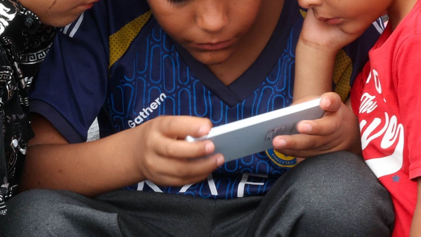 Niños observan un videojuego en el celular, durante su asistencia a la Basílica de Guadalupe en julio 2025. Foto: Cuartoscuro | Archivo