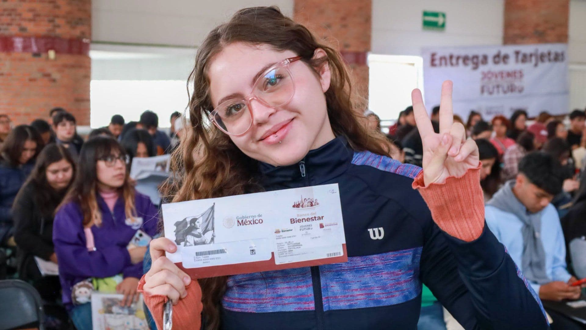 Jovencita posa con sobre donde está Tarjeta en entrega de Tarjetas de Jóvenes Construyendo el Futuro.
