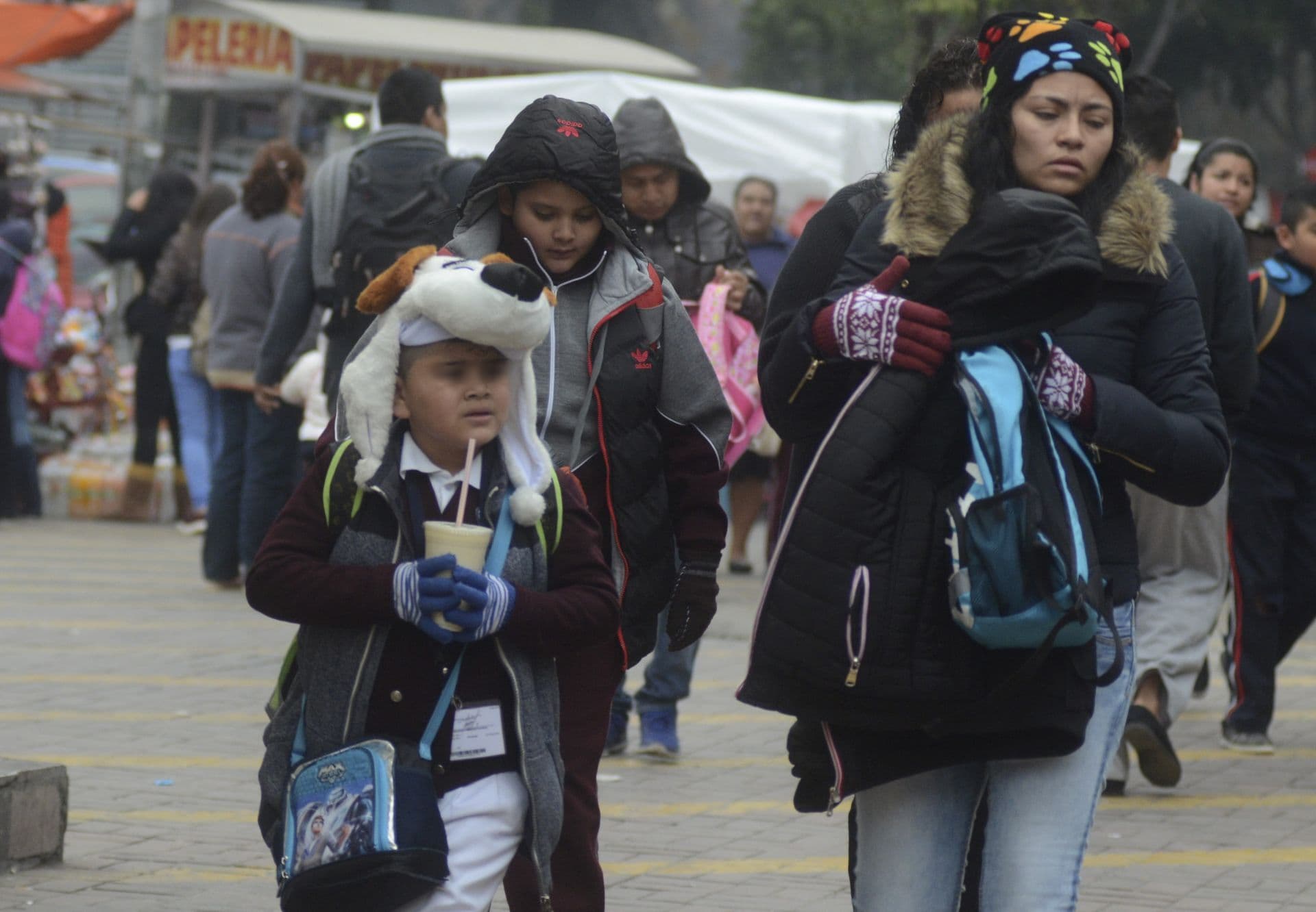 Madre e hijo caminan a la escuela con chamarras y gorros ante bajas temperaturas