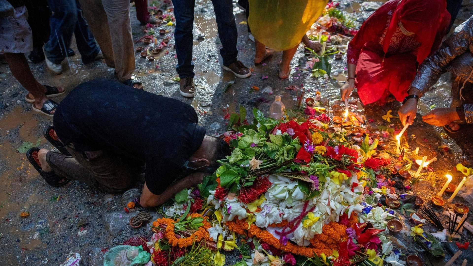 Hombre reza tras depositar una vela y flores en el lugar de enterramiento colectivo luego de inundaciones repentinas en Nepal. Foto: Reuters