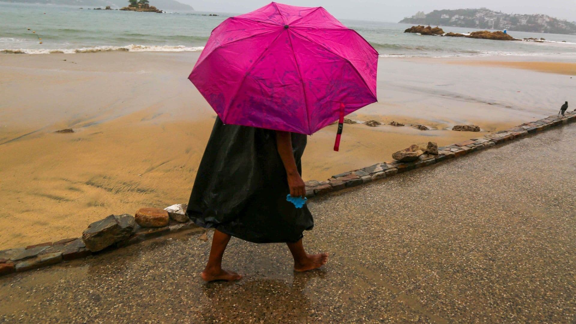 Una mujer camina con una sombrilla una tarde lluviosa en Acapulco