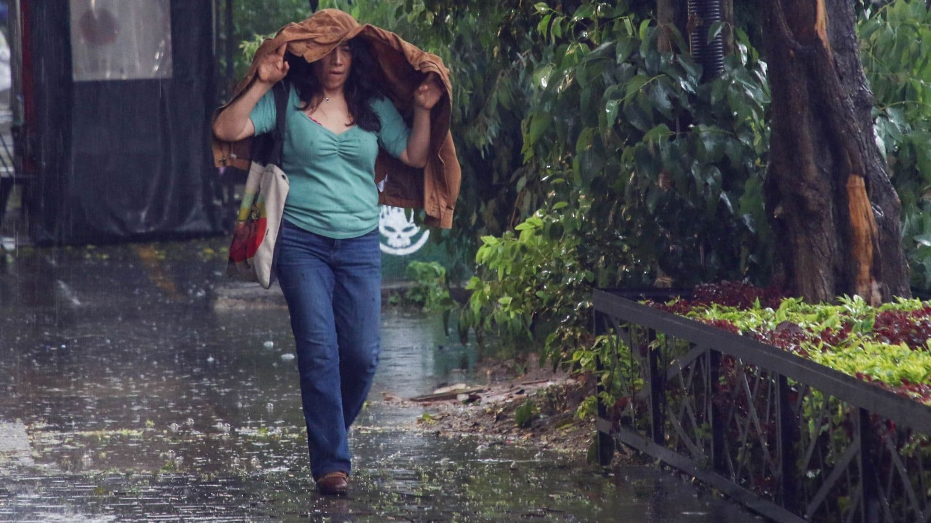 Una mujer se cubre con su abrigo de una lluvia en la Ciudad de México