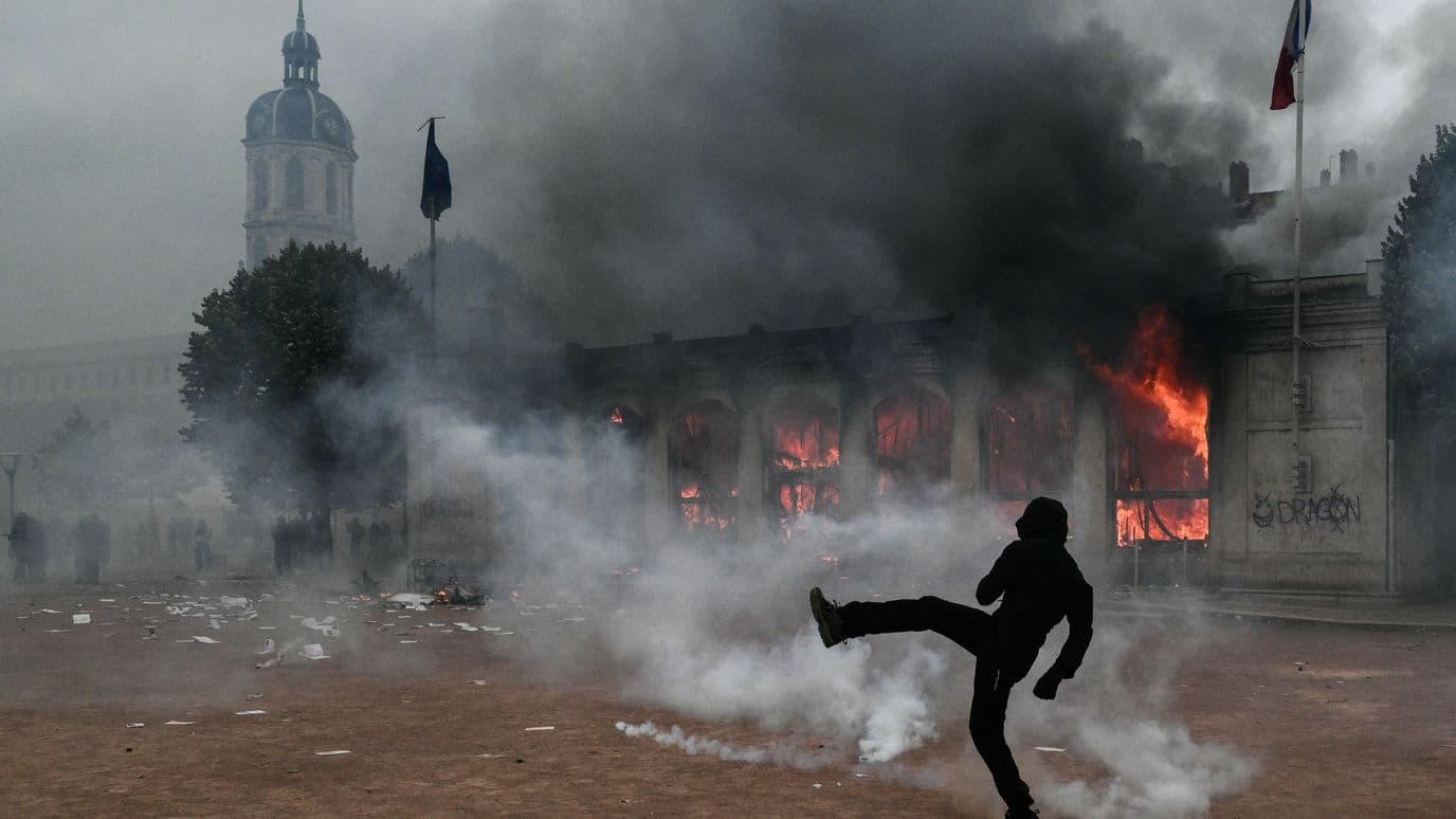 Un manifestante patea un proyectil mientras permanece en medio de gases lacrimógenos frente a la oficina de turismo de Lyon