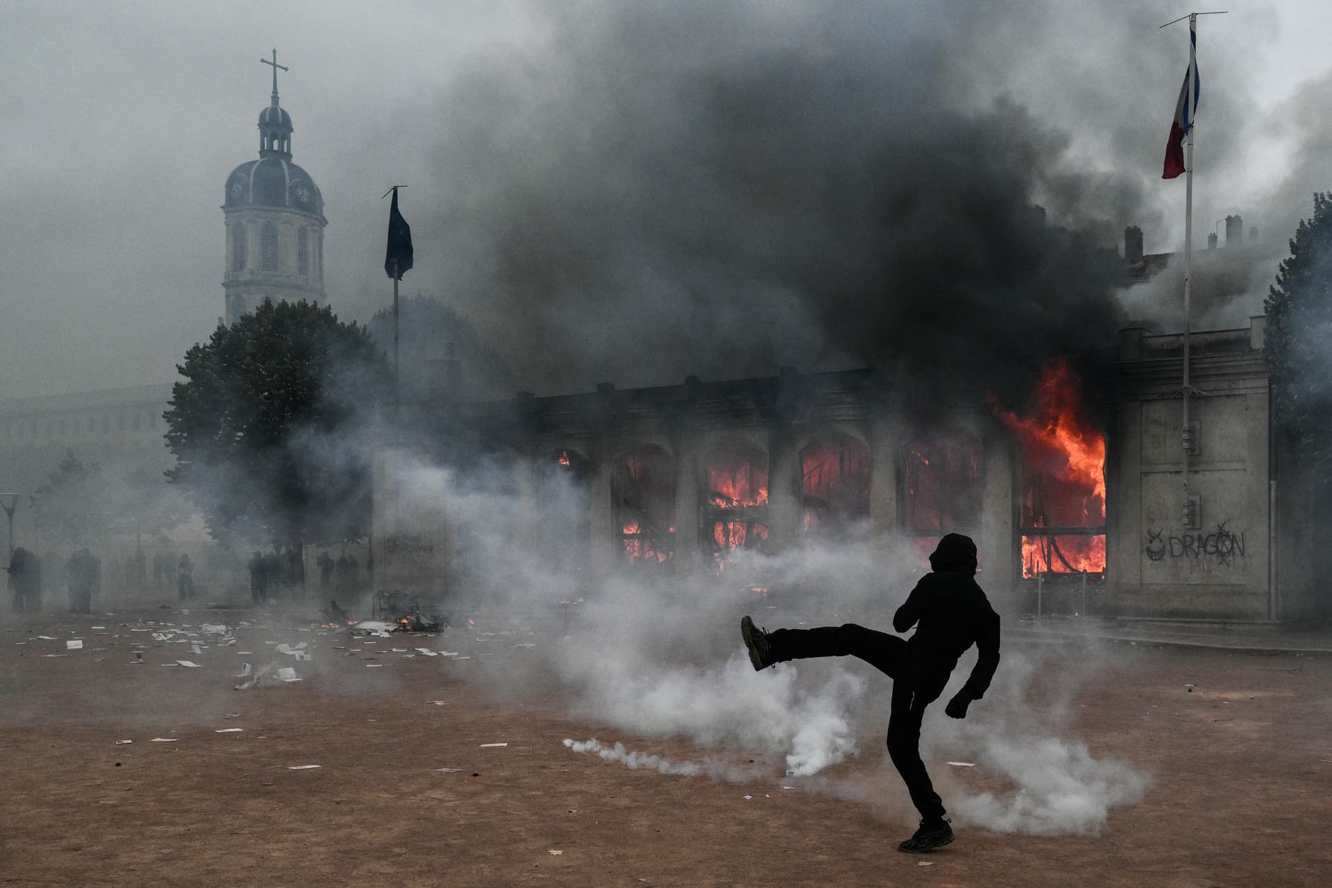 Un manifestante patea un proyectil mientras permanece en medio de gases lacrimógenos frente a la oficina de turismo de Lyon