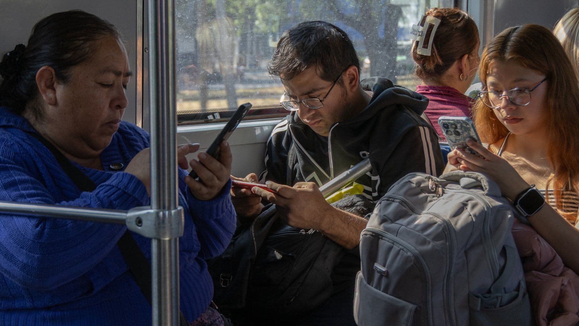 Personas viajando en el transporte público usan sus celulares.