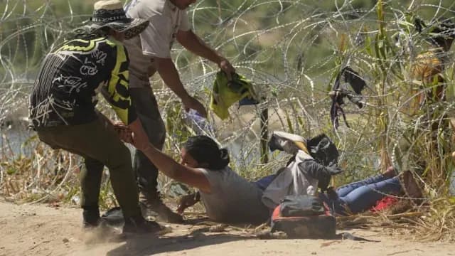 Una migrante que cruzó a Estados Unidos desde México es auxiliada a pasar debajo de alambre de púas en el río Bravo. Foto: AP | Archivo