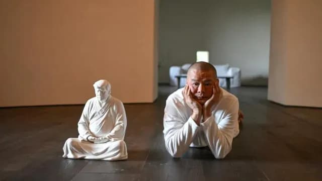 El artista Hong Jinshi posa junto a su creación, un Trump budista, en su taller