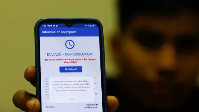 Migrantes que buscan asilo en EE. UU. utilizan sus teléfonos para solicitar una cita en un puerto de entrada terrestre.