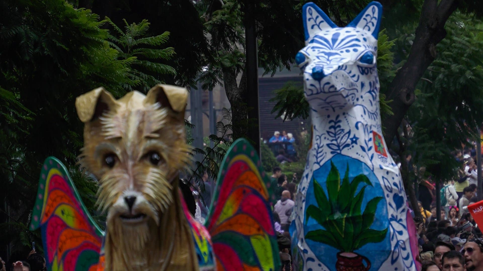 Un alebrije con forma de perro y alas de mariposa y otro blanco y azul con un agave avanzan detrás de músicos y bailarines. Foto: N+